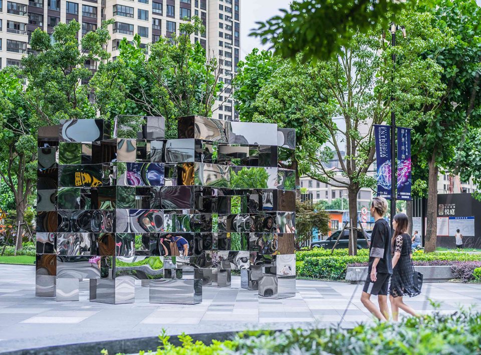 Stacked mirror-polished stainless steel cubes reflecting trees and passers-by on a Shanghai plaza, artwork by Arnaud Lapierre