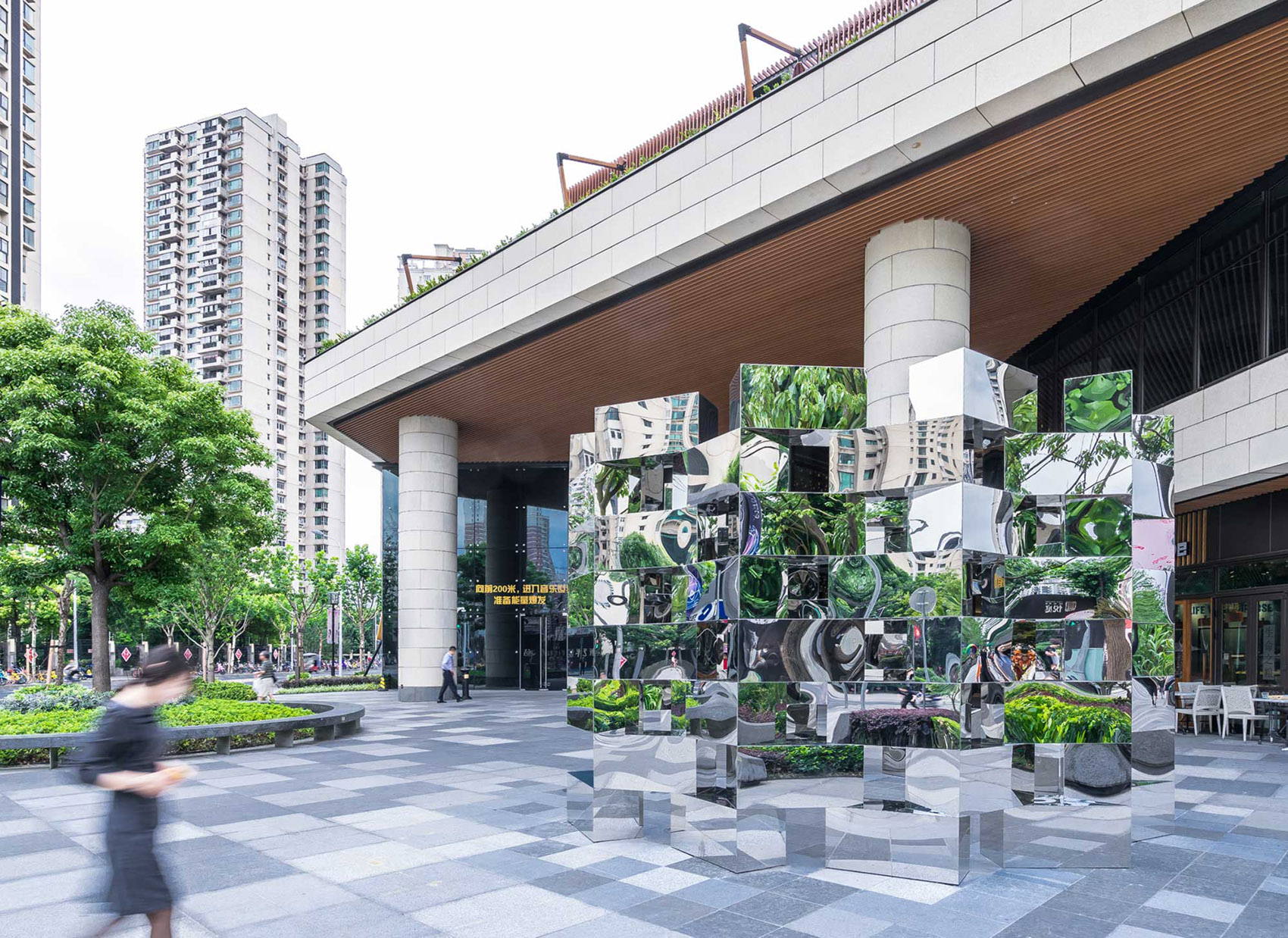 Mirror stainless steel cube sculpture at a building entrance plaza in Shanghai reflecting the surrounding landscape