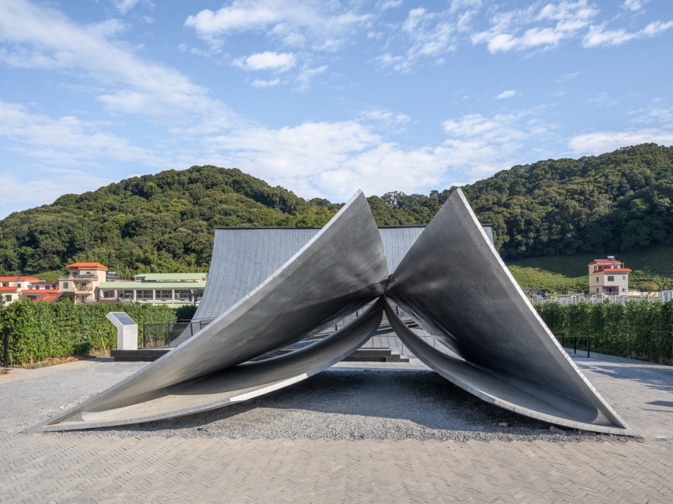 Pages Afloat by f-a-n: four curved stainless steel plates rising to a central ridge at Huizhou Village of Letters, with mountains behind