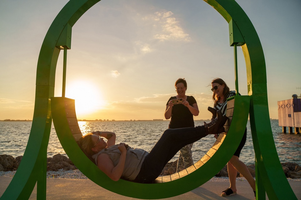Close-up of the curved wood-lined swing seat of Portal with a woman reclining and two people standing beside it
