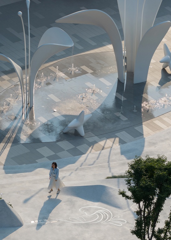 Curved white sculptural shells casting shadows across a water plaza in Yichang