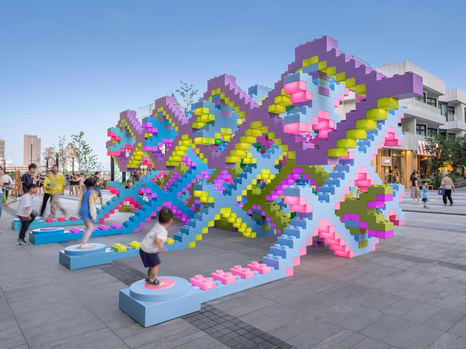 Children on the round jump pads beside Woven Playground, a woven lattice of oversized pastel bricks by Daxing Jizi Design in Shanghai