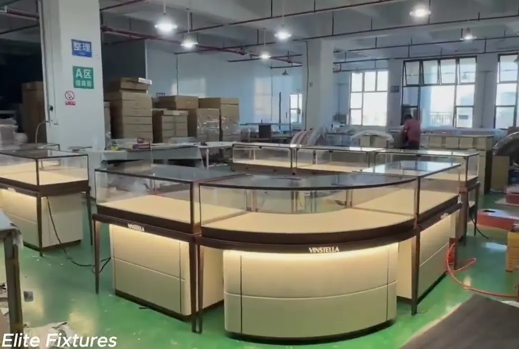 Curved glass jewelry display counters with LED-lit bases on the Elite Fixtures factory floor